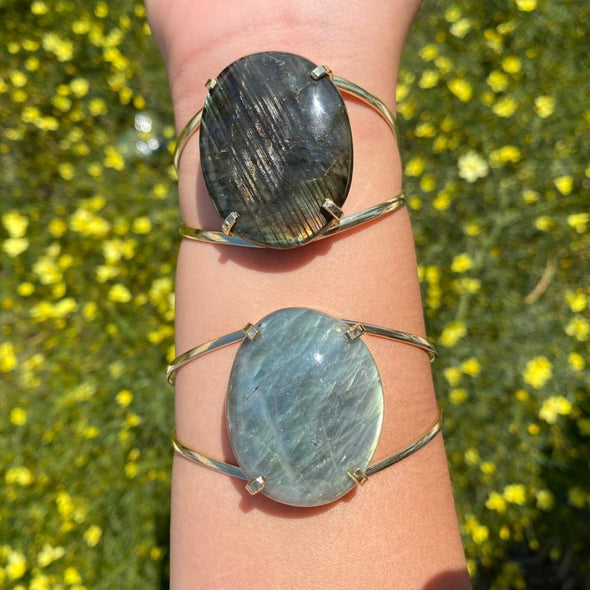 This cuff bangle bracelet features a large oval labradorite cabochon dark base color with metallic-looking color plays of blue, green, yellow, and red.